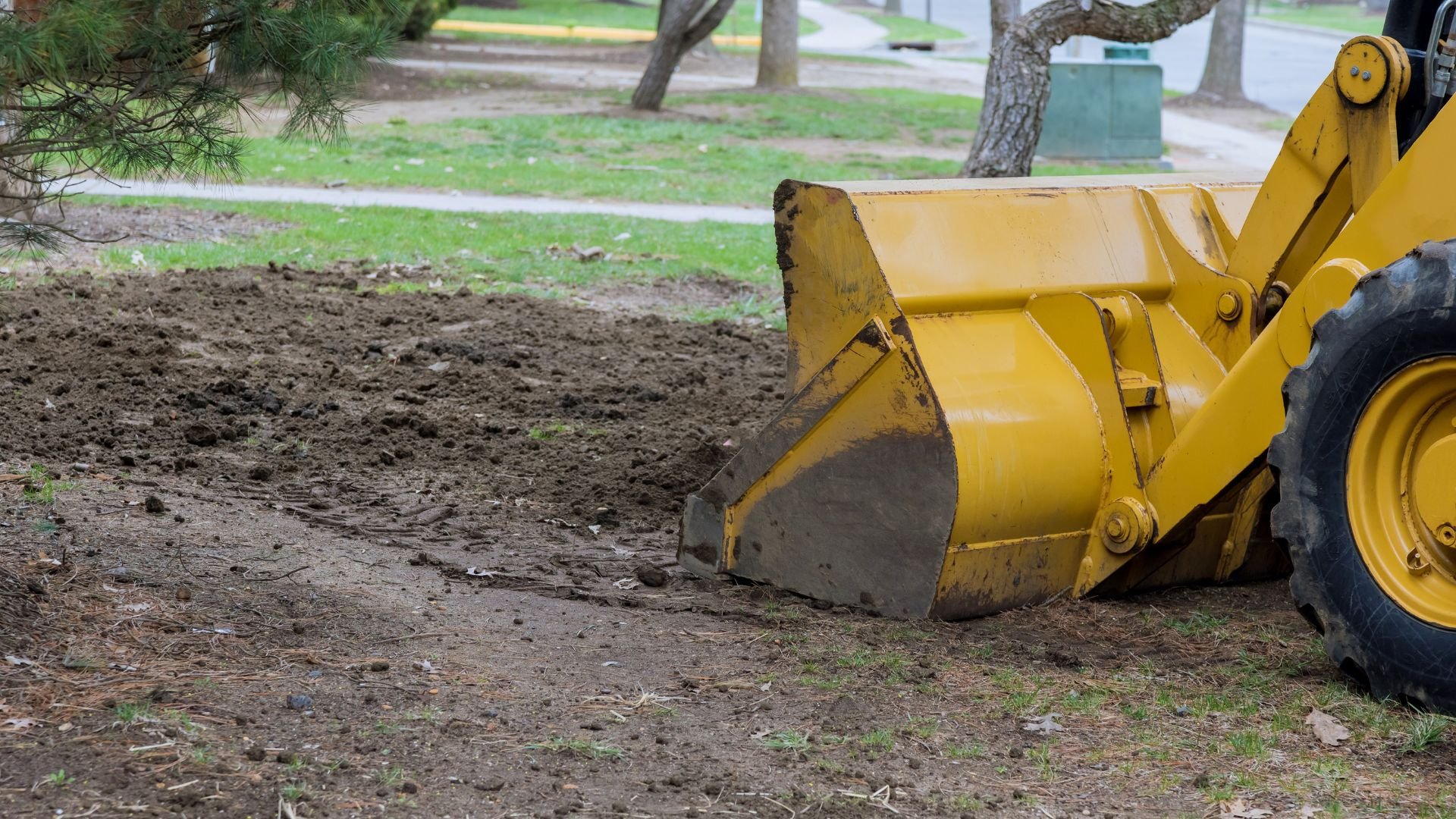 Yellow front-end loader digging in dirt near trees and grassy area